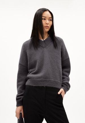 Grauer V-Ausschnitt-Pullover aus weichem, strukturiertem Material mit überschnittenen Schultern und gerippten Bündchen, kombiniert mit schwarzen Hosen, Vorderansicht.