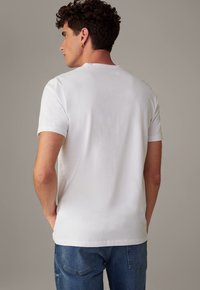 Weißes Baumwoll-T-Shirt mit kurzen Ärmeln, Rundhalsausschnitt und lockerer Passform. Getragen mit blauen Jeans aus Denim, die eine glatte Textur zeigen.