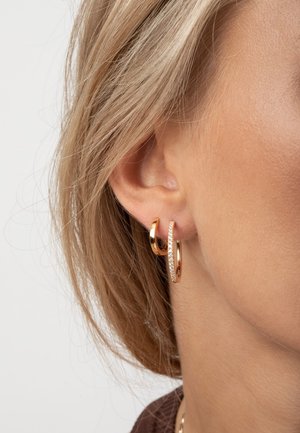 Guldörhängen med en slät yta och en mindre, texturerad hoop prydd med små klara stenar.