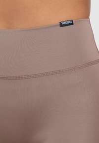 Leggings a vita alta di un colore mauve tenue, realizzati in tessuto liscio e elastico. Presentano un cinturino cucito con un piccolo tag nero.