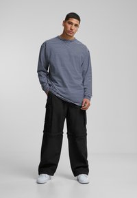 Long-sleeve, navy and white striped shirt with a crew neck, paired with loose black cargo pants and white sneakers. Simple, casual design.