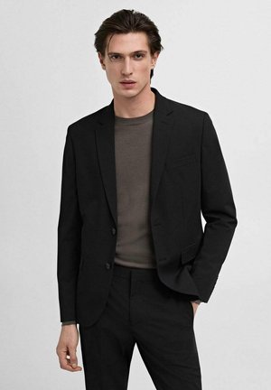 Black suit jacket with narrow lapels and two buttons, worn over a dark grey crew neck shirt. Features a single chest pocket and slim fit design.