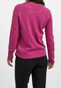 Ljusrosa, stickad tröja med rund halsringning och ribbade muddar och nederkant. Bakifrån visar den en avslappnad passform och mjuk textur.