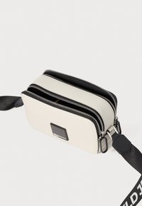 White leather crossbody bag with two zippered compartments, black accents, a logo patch, and a textured adjustable strap.