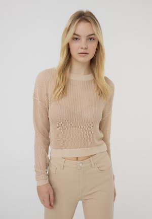 Maglione beige lavorato a maglia con una vestibilità larga, maniche lunghe e orlo a coste. Abbinato a pantaloni fitted beige chiaro, creando una palette di colori morbidi.