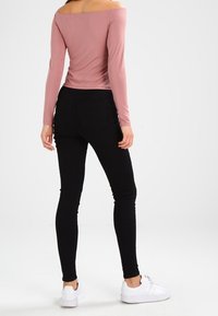 Halenka s dlouhým rukávem a odhalenými rameny ve vybledlé růžové barvě, zkombinovaná s černými skinny džíny a bílými teniskami. Hladký materiál, přiléhavý střih.