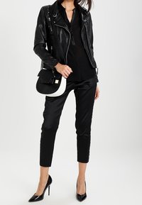 Veste de moto en cuir noir, blouse noire ajustée, pantalon noir sur mesure et escarpins pointus. Sac à main avec des accents noir et blanc.