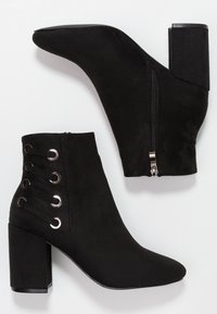 Botas negras hasta el tobillo de ante con punta afilada, tacón cuadrado, cremallera lateral y cordones decorativos con ojales en el lado exterior.