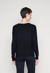 Maglione nero a maglia con vestibilità ampia, scollo largo e maniche lunghe. Presenta una texture liscia e polsi e orlo a costine.
