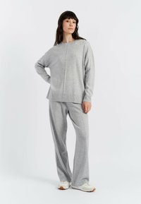 Grauer Strickpullover und passende Hose mit entspannter Passform, langen Ärmeln und gerippten Säumen, getragen mit weißen Sneakers.