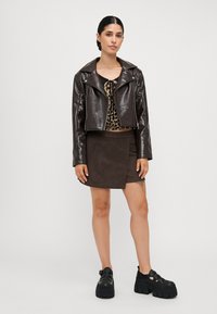 Brun kunstskinn cropped jakke med store revers, en leopardmønstret topp, brun semsket skinn omslagskjørt, og chunky svarte platå sko.