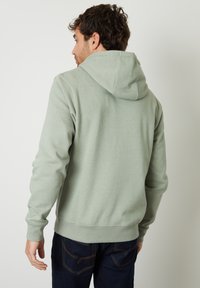 Lichtgroene hoodie met een zachte textuur, voorzien van een kangoeroezak en geribde manchetten, gecombineerd met donkere spijkerbroek.