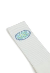 Vit ribbad strumpa med en oval design av en blå och gul "VANS"-logotyp. Mjuk textur, elastisk mudd och standard strumptyp.