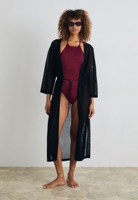 Must mustristile oomakate, pikkade varrukatega, lahtise istuvuse ja avatud esiosaga, millel on vöö koht, sobitatud Burgundia ujumiskostümiga.