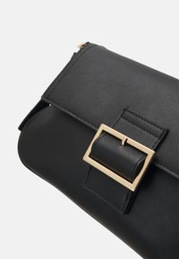 Pochette en cuir noir avec une fermeture en boucle en métal doré, design épuré et texture lisse. Comprend des accents cousus et une fermeture éclair.