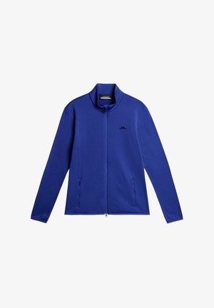 Blå ziptröja i slät tyg, med hög krage och två sidofickor med dragkedja, samt en liten svart logotyp på bröstet.