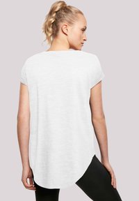 Hvit kortermet skjorte med rund nederkant, laget av et mykt, strukturert stoff og en løs passform, kombinert med svarte leggings.