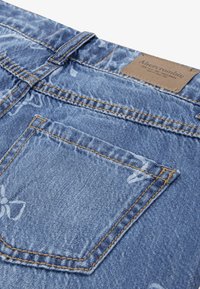 Kameran izbliza na stražnji džep plavih traperica s uzorkom leptira i smeđom kožnom oznakom brenda Abercrombie.