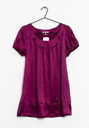 Blouse violette brillante à manches courtes avec un col rond et des détails froncés, suspendue sur un cintre noir sur fond blanc.
