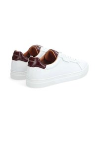 Baskets en cuir blanc avec des accents de talon texturé bordeaux et une doublure intérieure beige. Elles présentent une semelle en caoutchouc plate et un design perforé.