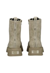 Botines beige con un acabado similar al ante, que cuentan con una suela gruesa, cierre con cremallera y una pestaña con el logo en relieve en la parte posterior.