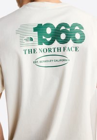 Camiseta blanca con texto y logo verde "1966 The North Face Est. Berkeley California" en la espalda, llevada por una persona de espaldas.