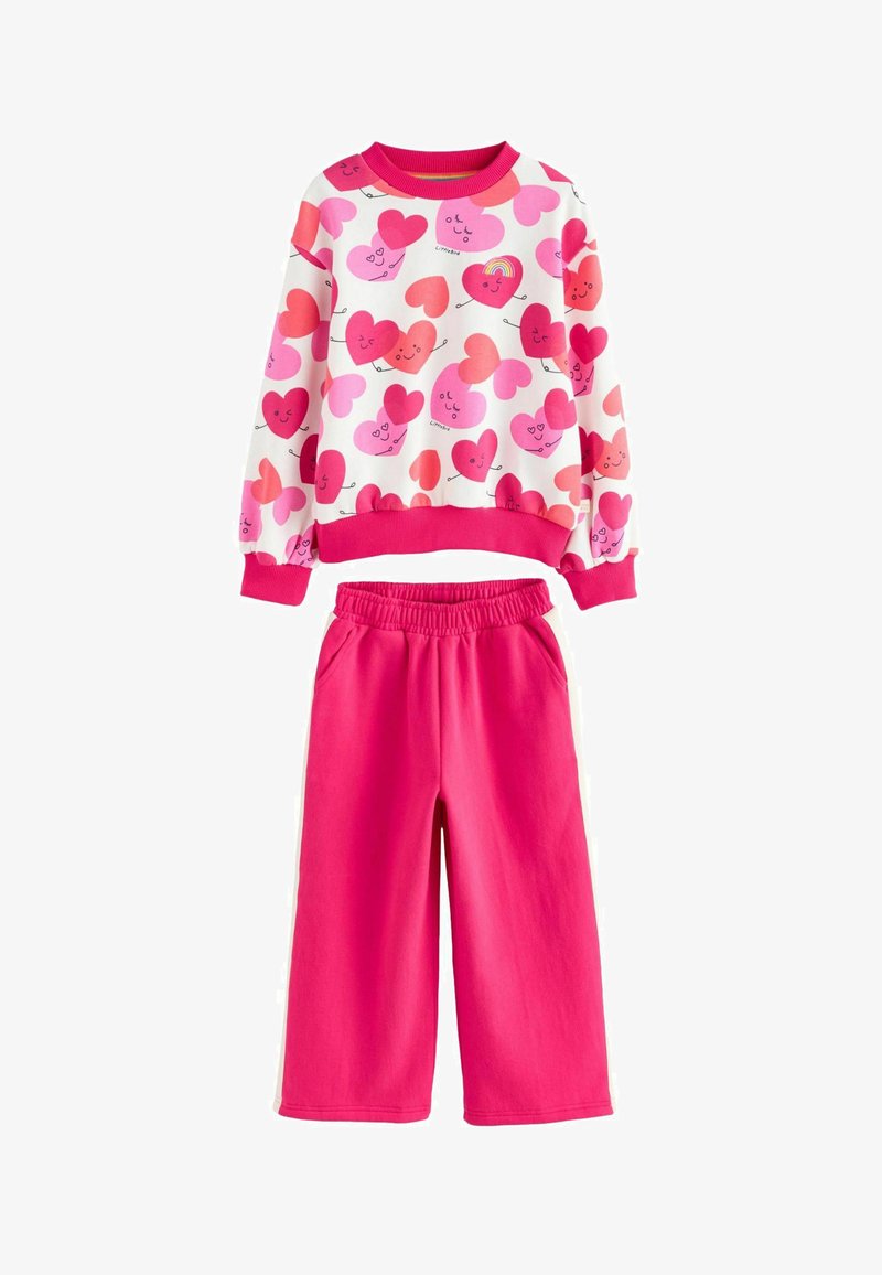 Tricou și pantaloni de trening. Bluza albă cu modele de inimioare roz; manșete striate. Pantaloni roz aprins cu talie elastică și buzunare laterale.