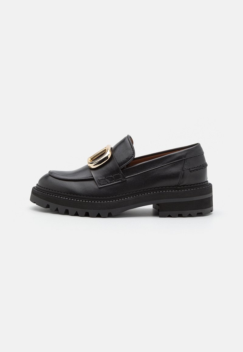 Mocassin en cuir noir avec semelle épaisse à crampons et grande boucle rectangulaire dorée sur la bride, présenté en profil latéral sur fond blanc.