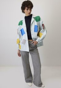 Svijetloplava košulja s dugim rukavima s raznobojnim kvadratnim aplikacijama u zelenoj, žutoj, plavoj, smeđoj i sivoj boji; uparena sa sivim širokim hlačama i crnim topom.