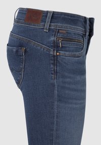 Mörkblå denimjeans med smal passform, med en bakficka och en zippered ficka framtill. Brun läderlapp på midjan.