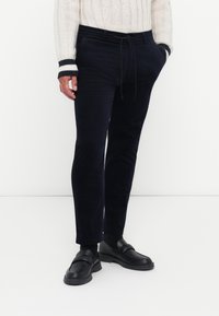 Marineblauwe corduroy broeken met een trekkoord in de taille, voorzien van een slim fit en een soepele textuur. Gecombineerd met zwarte instap schoenen.