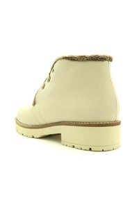 Botines de imitación de cuero color crema con punta redondeada y suela de goma marrón. Presentan un suave collar forrado de piel sintética y un cierre de cordones en la parte frontal.