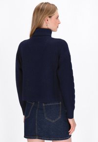 Marineblaues, kürzes Sweatshirt mit strukturiertem Strick und hohem Kragen, kombiniert mit einem Rock aus dunklem Denim mit Gesäßtaschen.