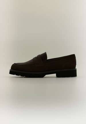 Mocassin en cuir marron foncé avec une bride sur le dessus et une semelle épaisse en caoutchouc noir, vu de côté sur un fond clair.