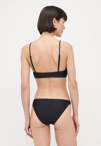 Zwart bikiniset met een eenvoudig ontwerp, dunne bandjes, verstelbare sliding en contrasterende gele stiksels aan de randen.