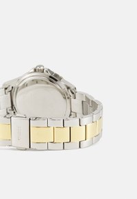 Sølv- og guldtonet metalur med en dual-tone armbånd og en rund urskive, der fremviser en poleret finish og en spænde-lukning.