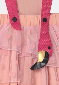 Robe rose avec des bretelles en filet texturé, jupe en tulle à pois superposés et accent flamant rose noir et or sur les bretelles.