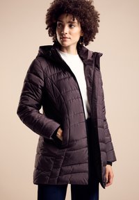 Lila pufferjacka med quiltat mönster, dragkedjestängning och huva. Har sidofickor och en mjuk textur. Bärs över en vit topp.