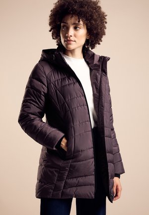 Paarse pufferjack met een geborduurde patroon, ritssluiting en een capuchon. Voorzien van zijzakken en een zachte textuur. Gedragen over een wit shirt.
