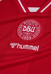 Czerwona sportowa koszulka z logo Dansk Boldspil-Union (DBU) z "1889" oraz białym logo marki Hummel pod kołnierzem.