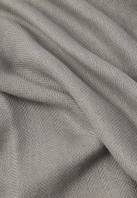 Šedá tkanina tkaná v herringbone vzore, ktorá ukazuje hladkú textúru a jemný lesk, prehnutá, aby odhalila hĺbku a rozmer.