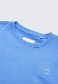 Felpa blu con collo rotondo, texture morbida e un piccolo ricamo di una faccina sorridente bianca sul davanti. Design minimalista.