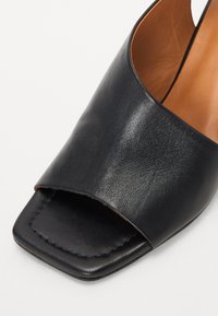 Mule ouverte en cuir noir avec une large bande et un devant carré, dotée d'un intérieur lisse couleur tan.