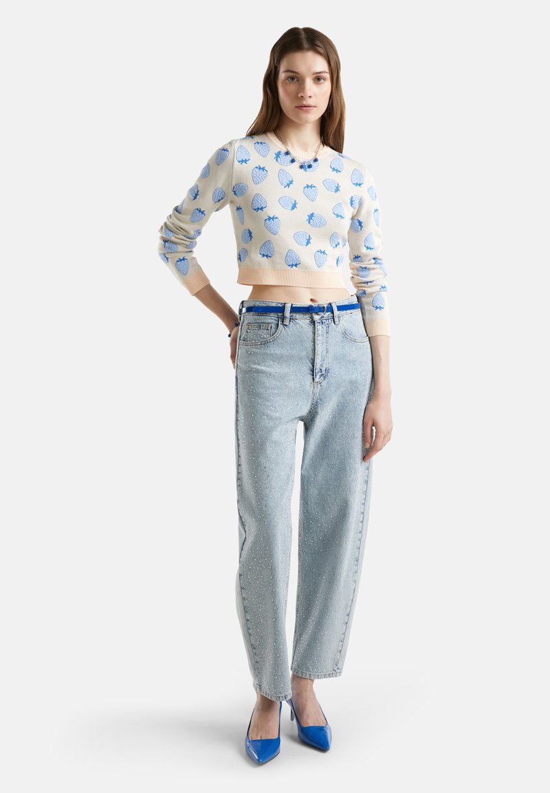 Kremowy sweter z niebieskim wzorem muszli, w połączeniu z jasnoniebieskimi jeansami z wysokim stanem ozdobionymi detalami oraz niebieskimi czółenkami.