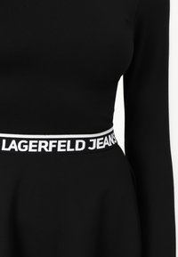Black long-sleeve dress featuring a fitted bodice and a flared skirt. Waistband displays "LAGERFELD JEANS" in white on a black background.