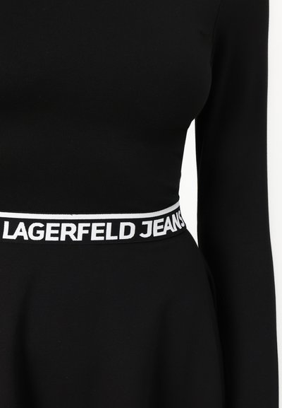 Robe noire à manches longues avec un corsage ajusté et une jupe évasée. La taille présente "LAGERFELD JEANS" en blanc sur fond noir.