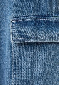 Ljusblå denimtyg med en lappficka med synlig sömnad. Texturen är något grov, med ett klassiskt vävmönster.