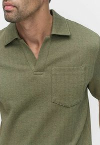 Oliivivihreä neulepolo paita, jossa on herringbone-kuvio, V-pääntie ja vasemmalla puolella rintatasku; kangas on tekstuuriltaan mielenkiintoinen.