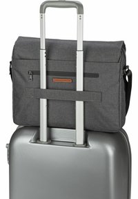 Bolsa de mensajería de tela gris asegurada sobre una maleta de plástico rígido plateada con mango telescópico, que presenta un bolsillo con cremallera y un acento de cuero.