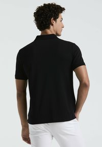 Zwarte poloshirt met korte mouwen en een klassieke kraag, gemaakt van een gestructureerde stof. Ontworpen met een rechte zoom en zijsplitten voor extra comfort.